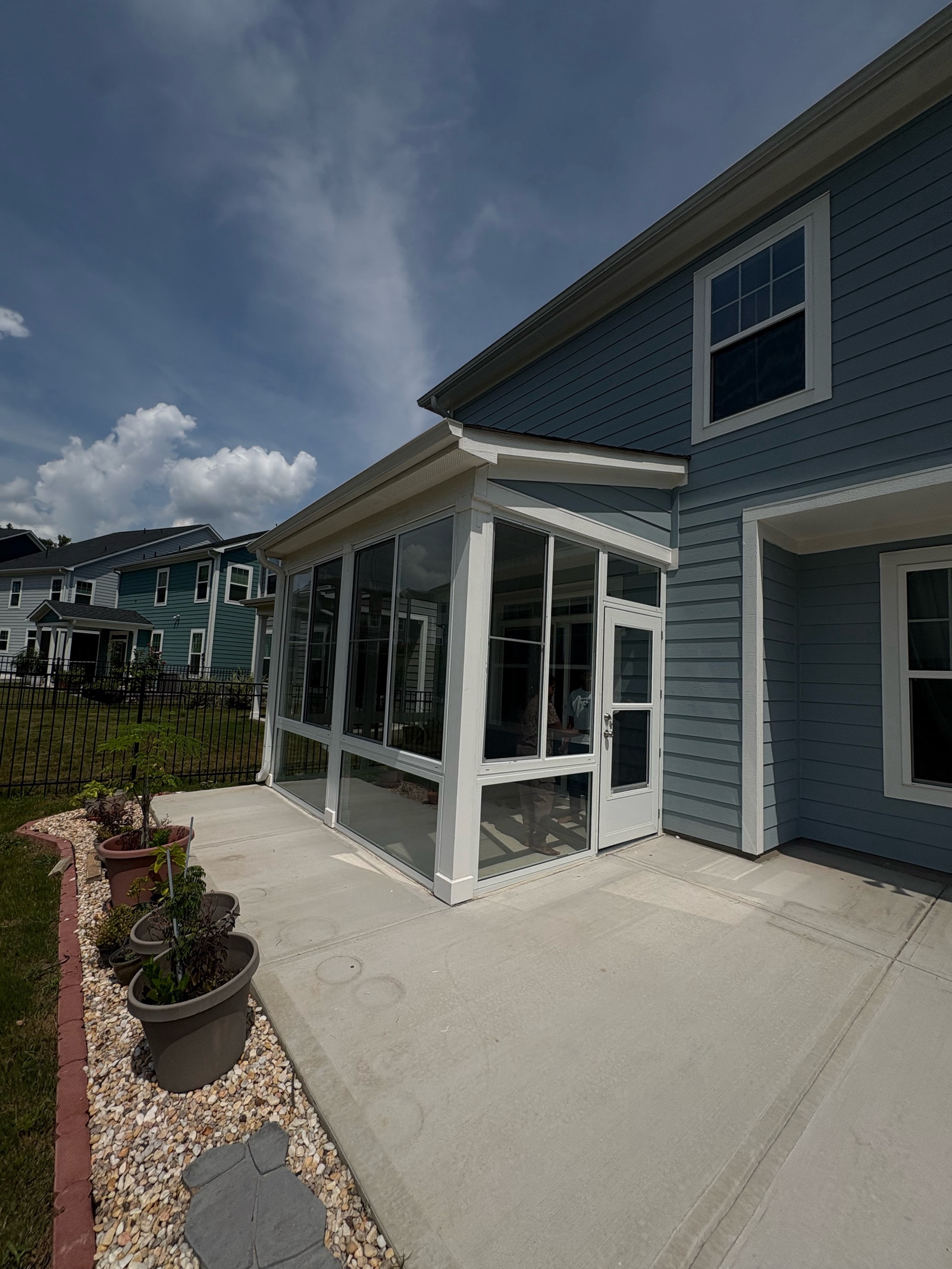 Angled exterior view of a white CWS porch enclosure with single-pane clear glass and a glass enclosure door.