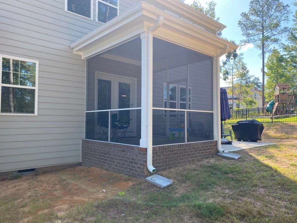 White extruded-aluminum screen enclosure on an elevated porch above a brick foundation.