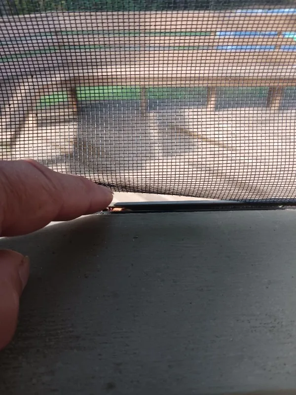 Damaged screen mesh separated near the edge of a framed opening.