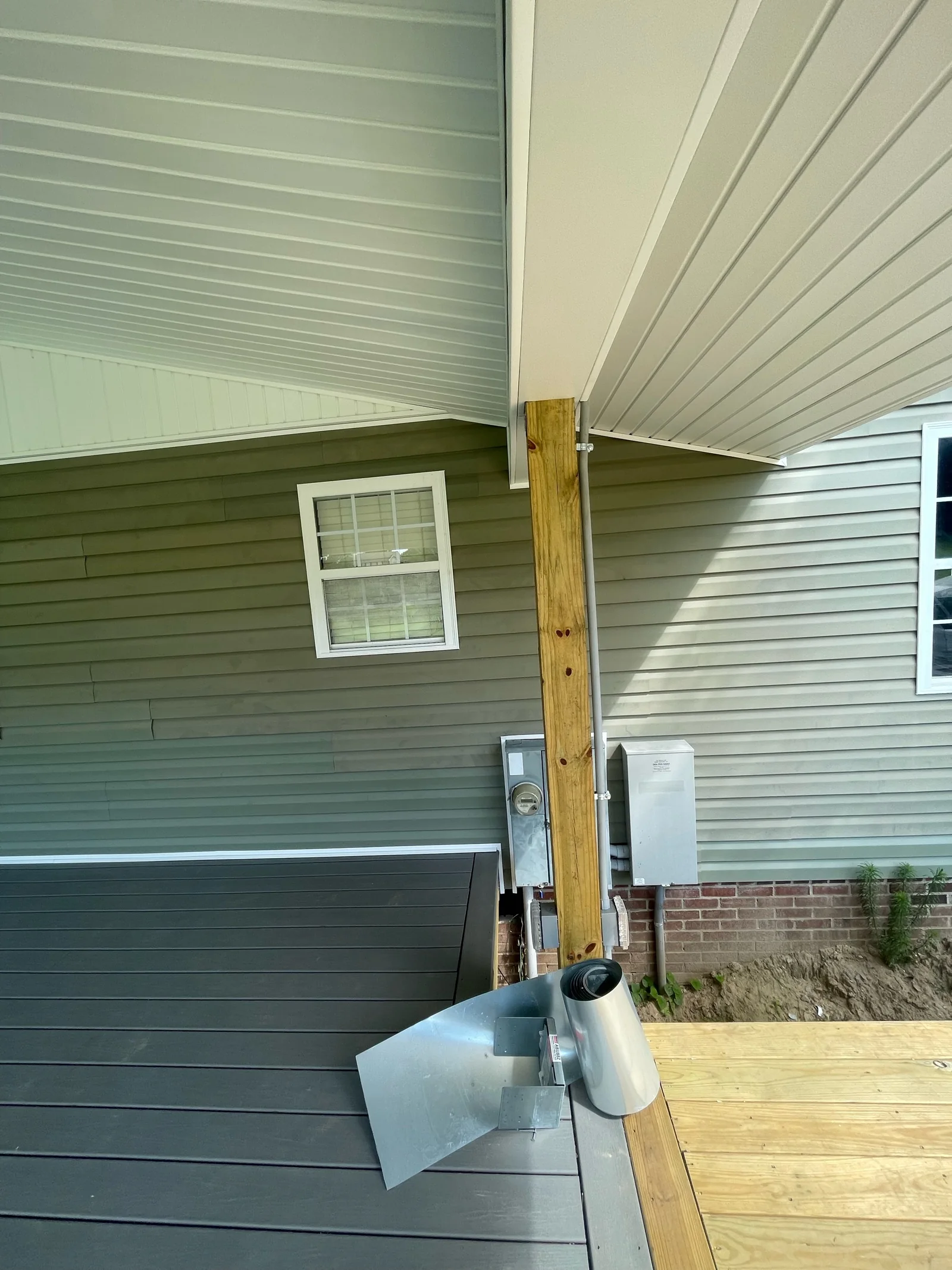 Porch-side view before a screen system is installed, showing a support post, wall-mounted utilities, roof and ceiling connections and deck edges.