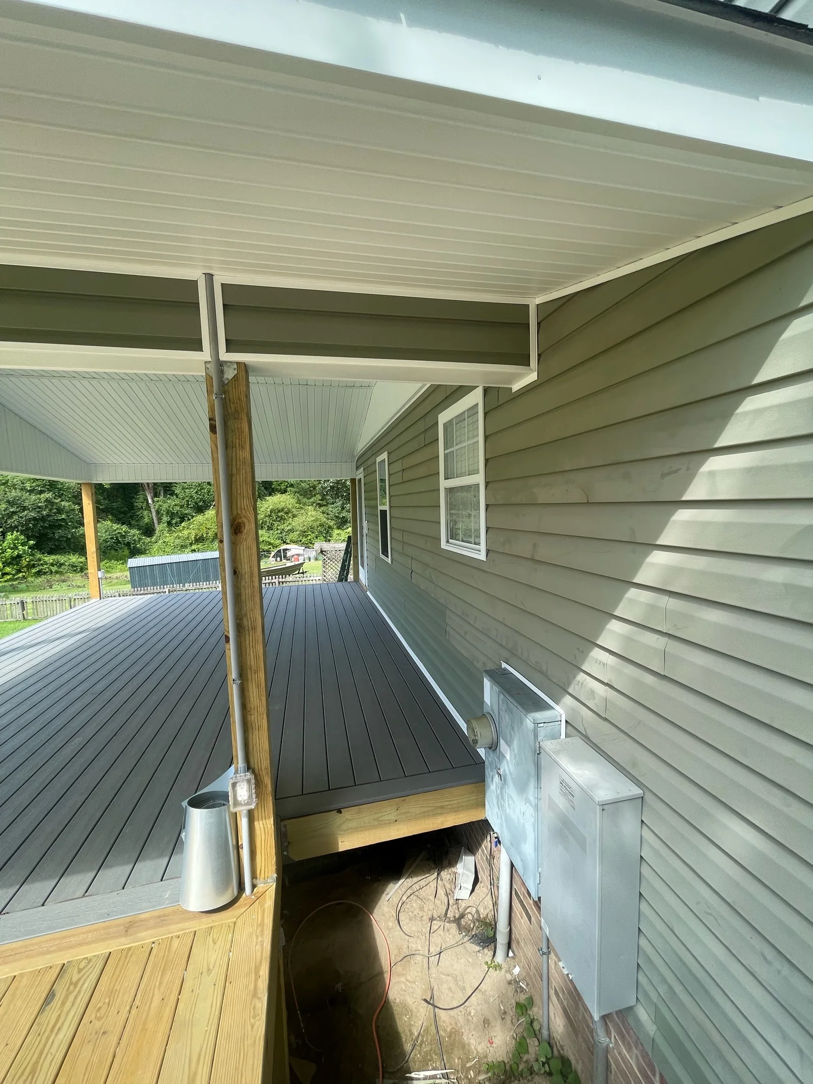 Side view of a covered porch before a screen system is installed, showing the deck transition, support post, exterior utilities and nearby access.