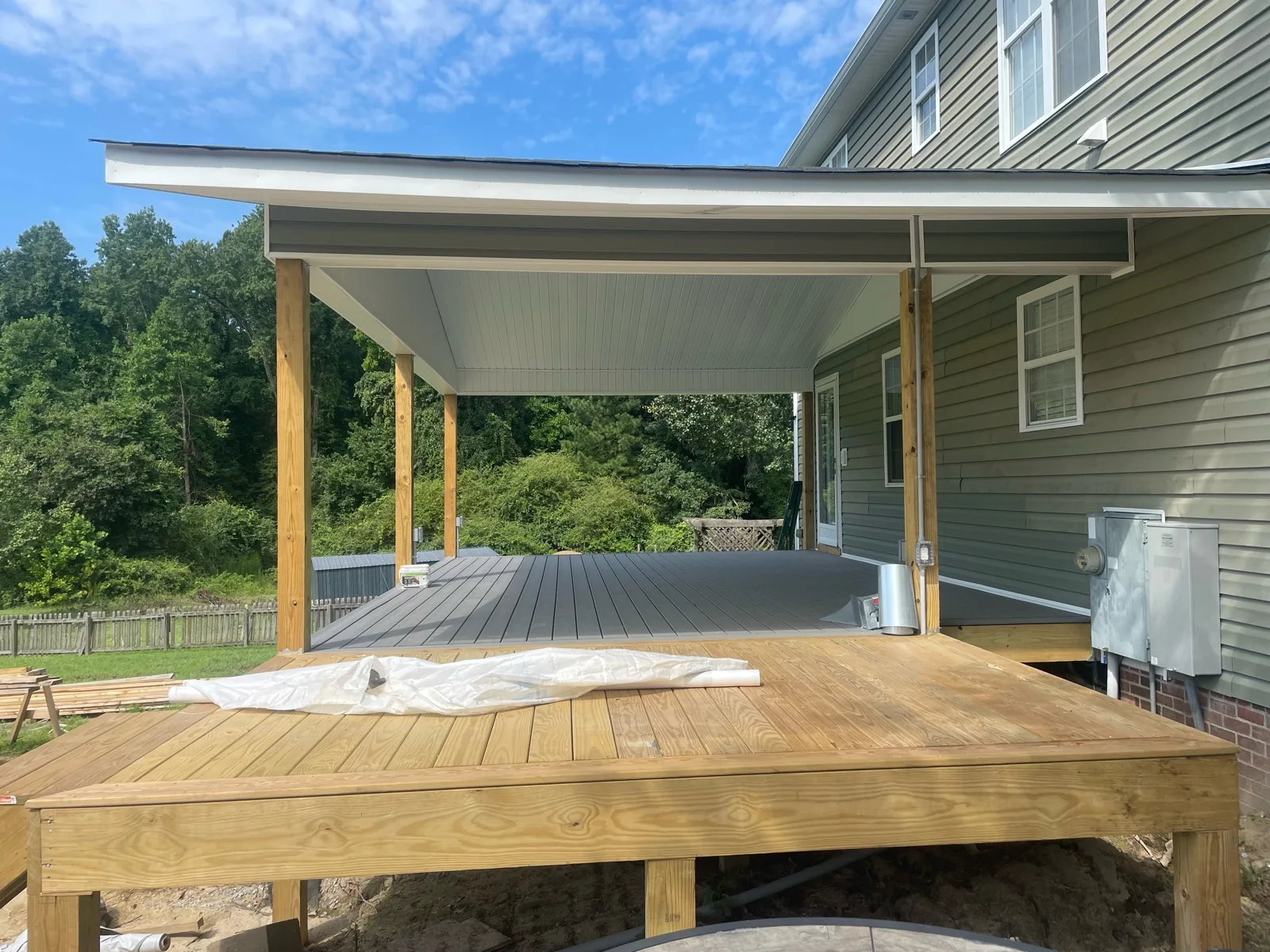 Wide view from the deck of a covered porch before a screen system is installed, showing the open wall, roof, ceiling, posts and walking path.