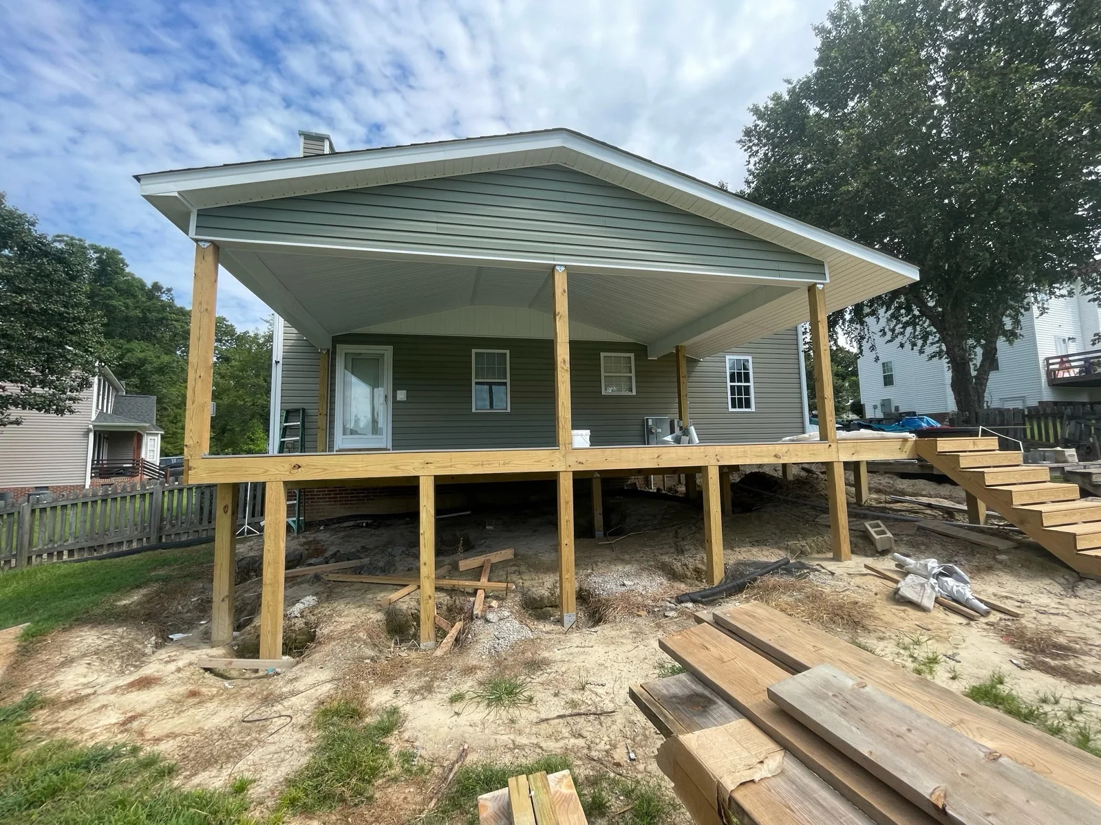 Wide front view of a covered porch before a screen system is installed, showing the open walls, posts, deck, stairs and surrounding grade.