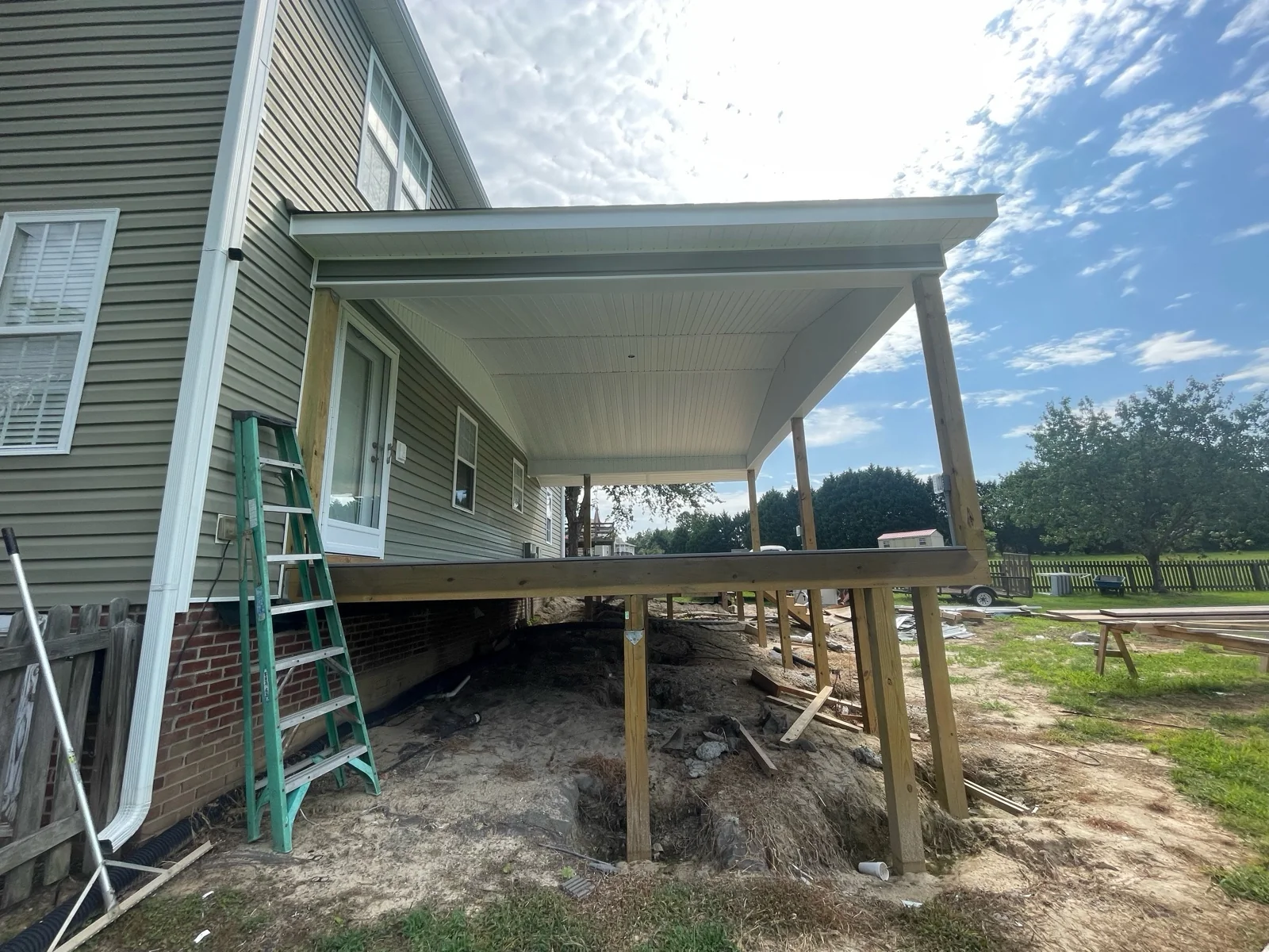 Wide side view of a covered porch before a screen system is installed, showing the raised deck, posts, roof connection and exterior access.