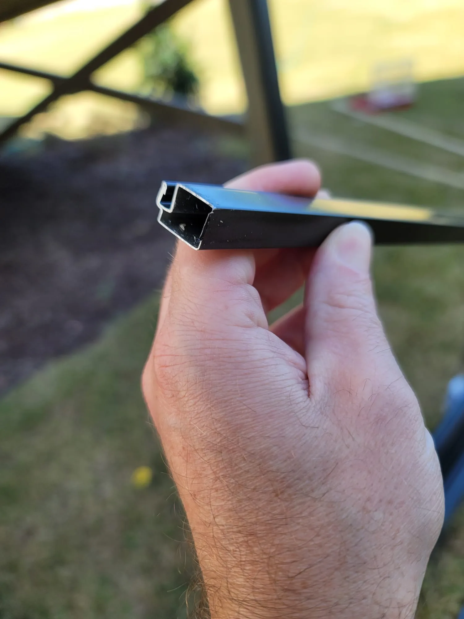 Hand holding the end of a black removable aluminum screen-panel frame to show its profile.