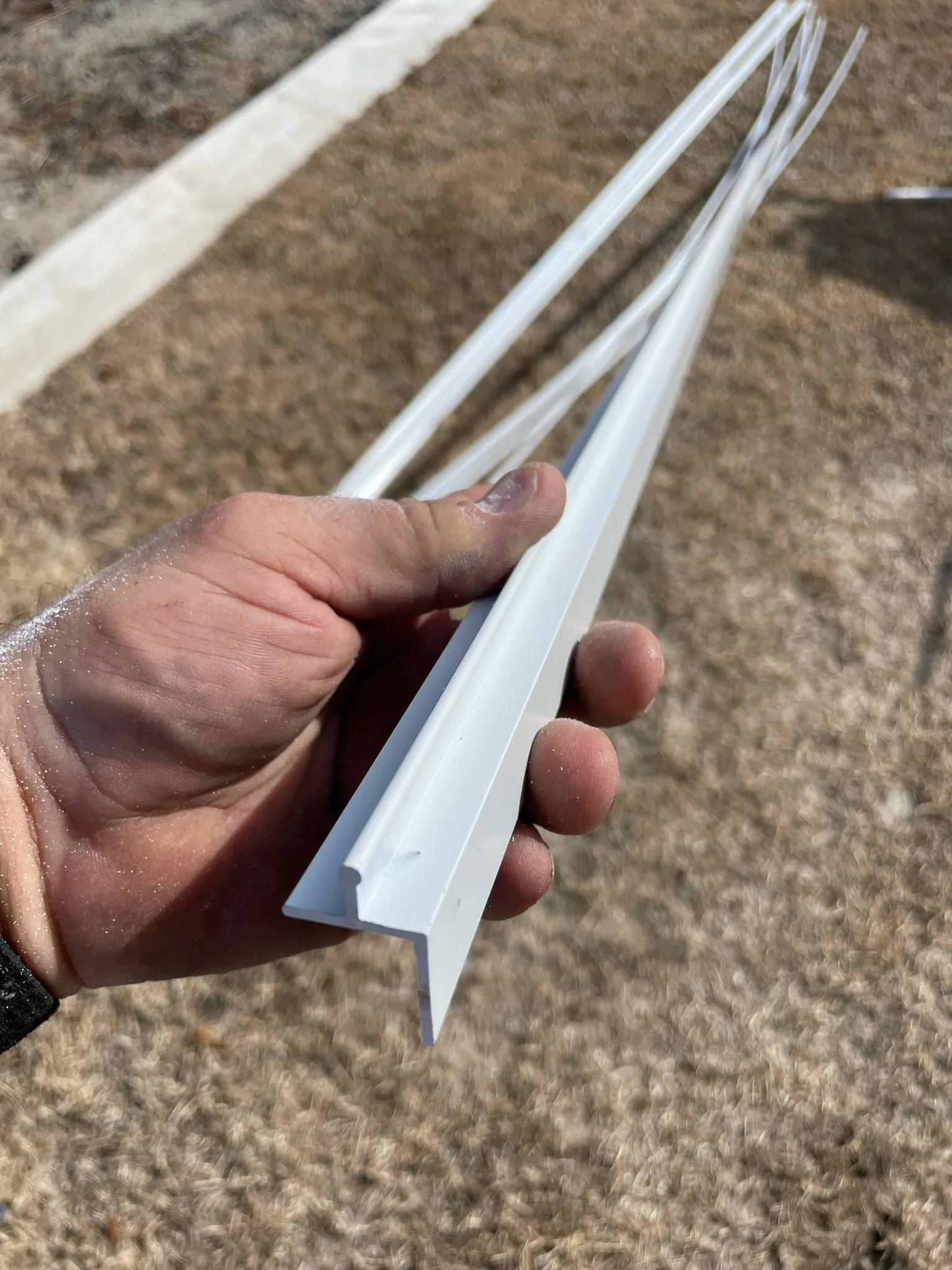 Hand holding the end of a white SCREENEZE aluminum base to show its profile.