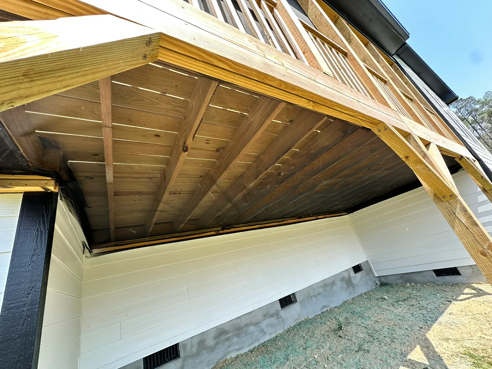 Screen mesh stapled beneath the joists of a raised wood porch.