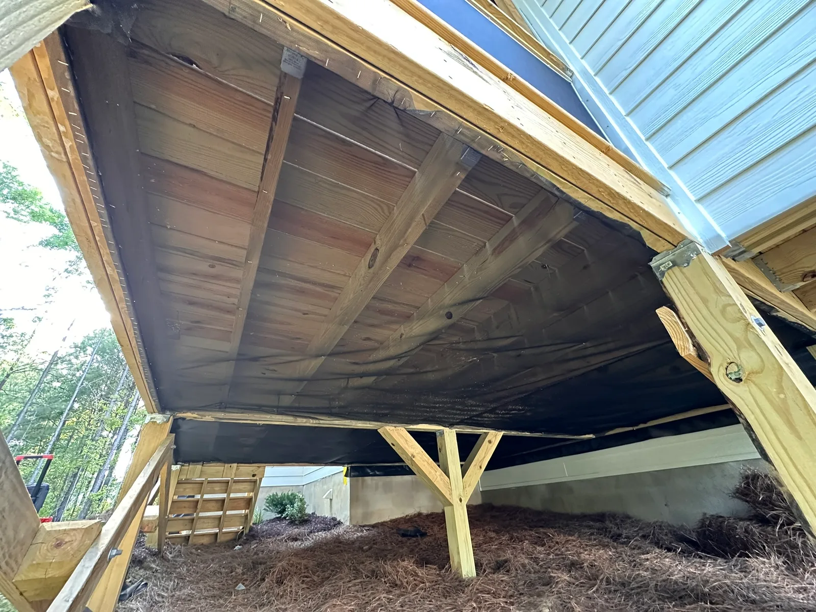 Screen mesh stapled beneath wood porch framing around posts and beams.